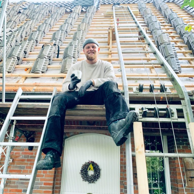 Dachdeckermeister Anton Krüger sitzt auf einem Gerüst nach abgeschlossener Dacharbeit