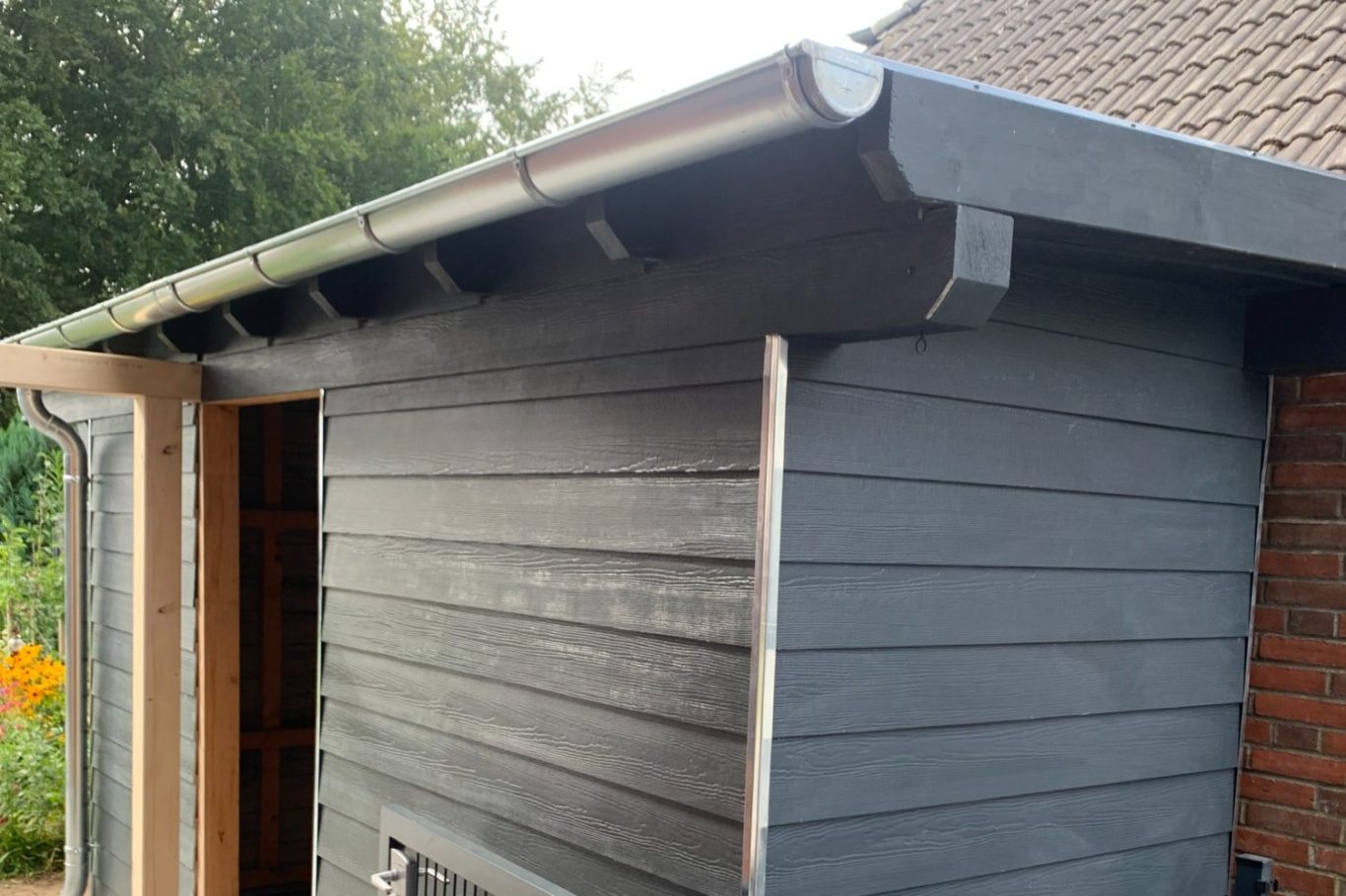 Dachkante eines Holzschuppens mit neuer Fassade grauer Farbe 